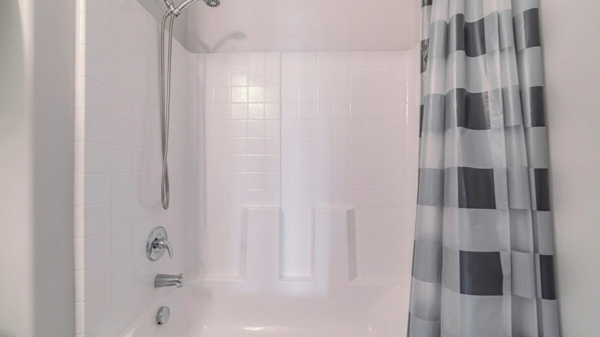 Bathtub with shower and open curtains in a white bathroom